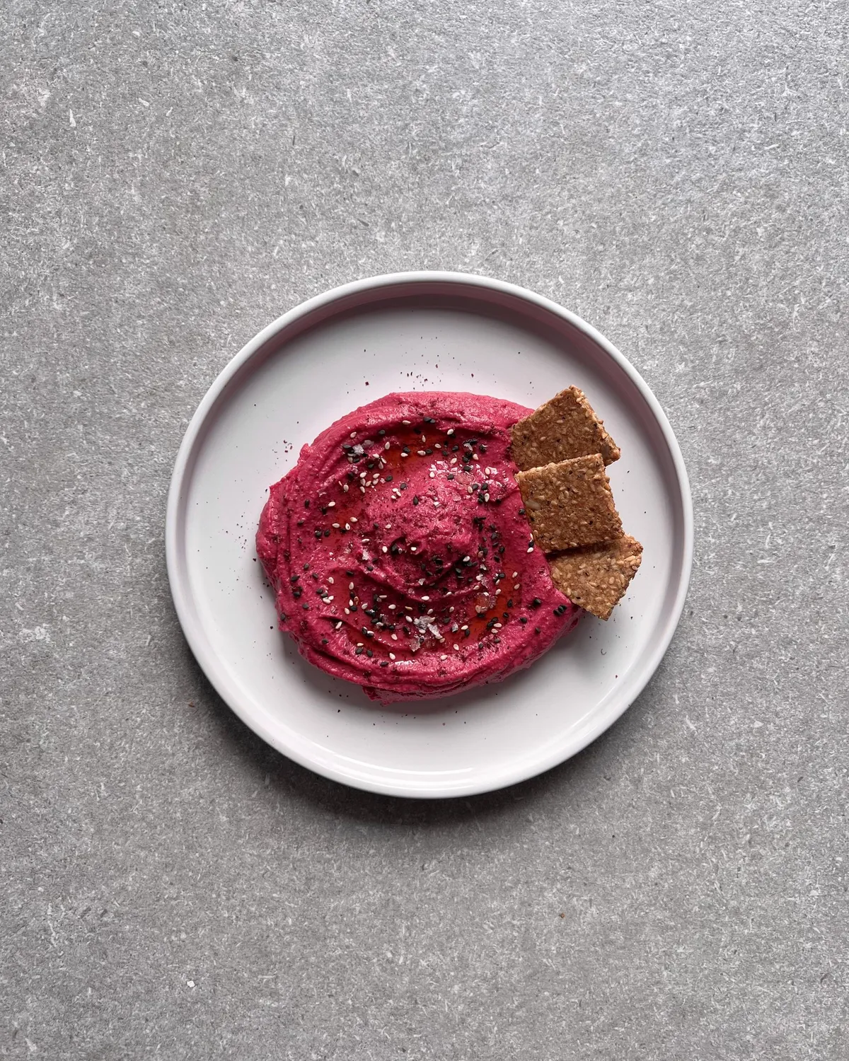 Bol d'hummus rosa de remolatxa amb llavors de sèsam i sal en escames, acompanyat de crackers