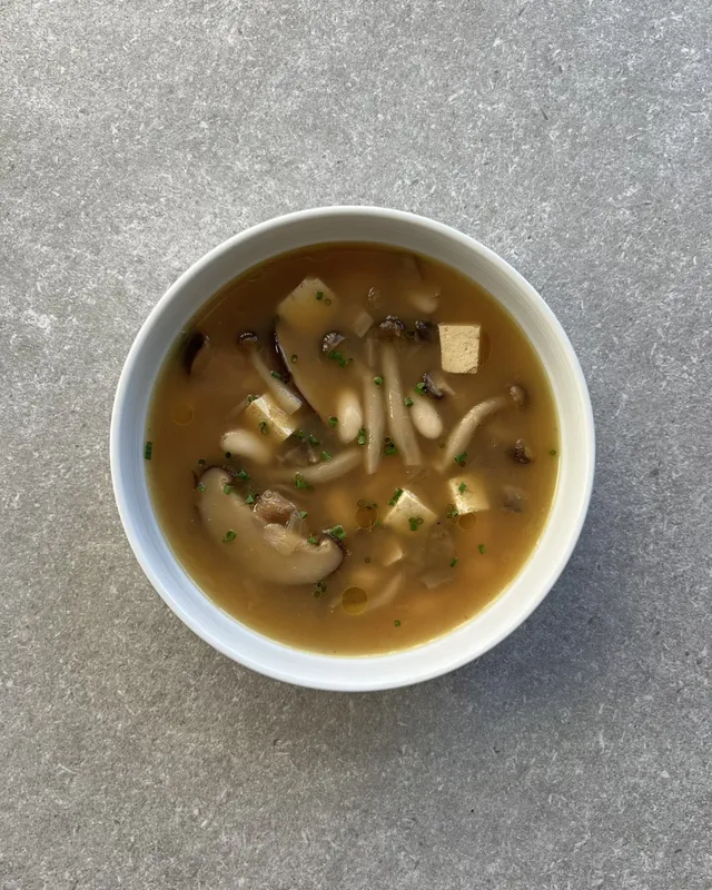 Bol blanc amb sopa de bolets, daus de tofu, mongetes blanques i cibulet picat